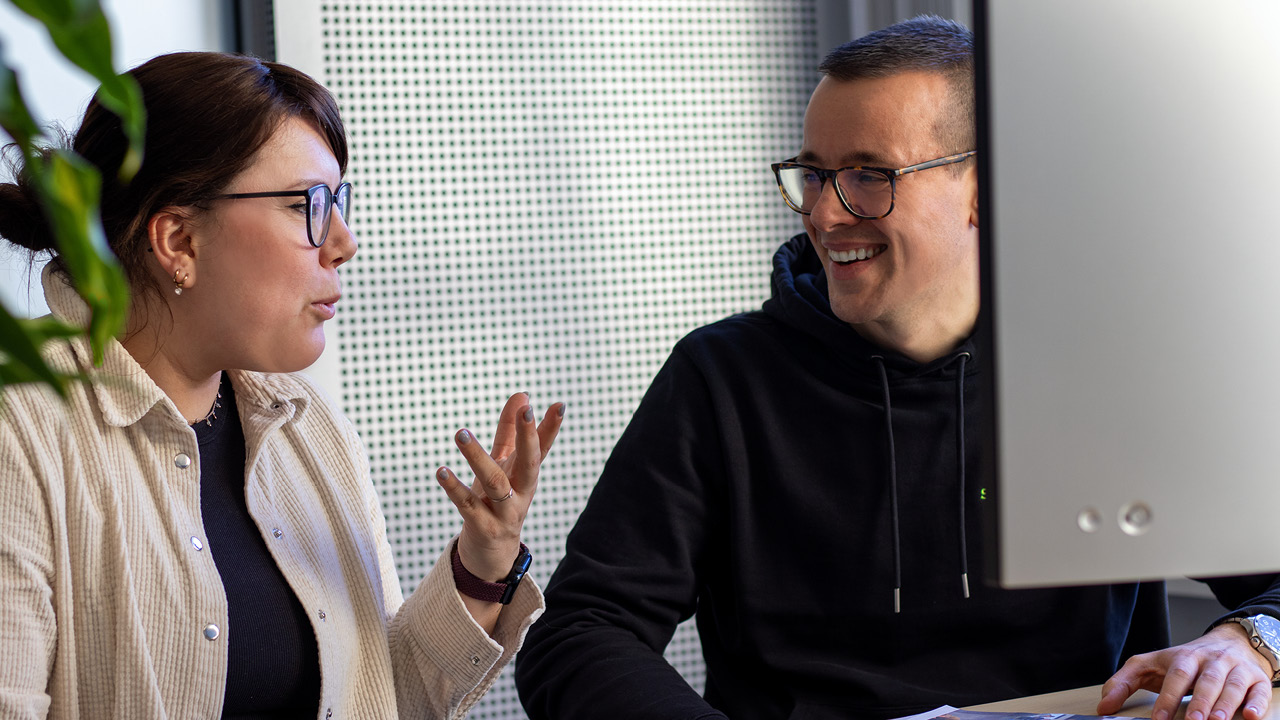 NeueBilder_Überuns_1280px_Teil2_11 zwei Personen im Büro, die sich unterhalten